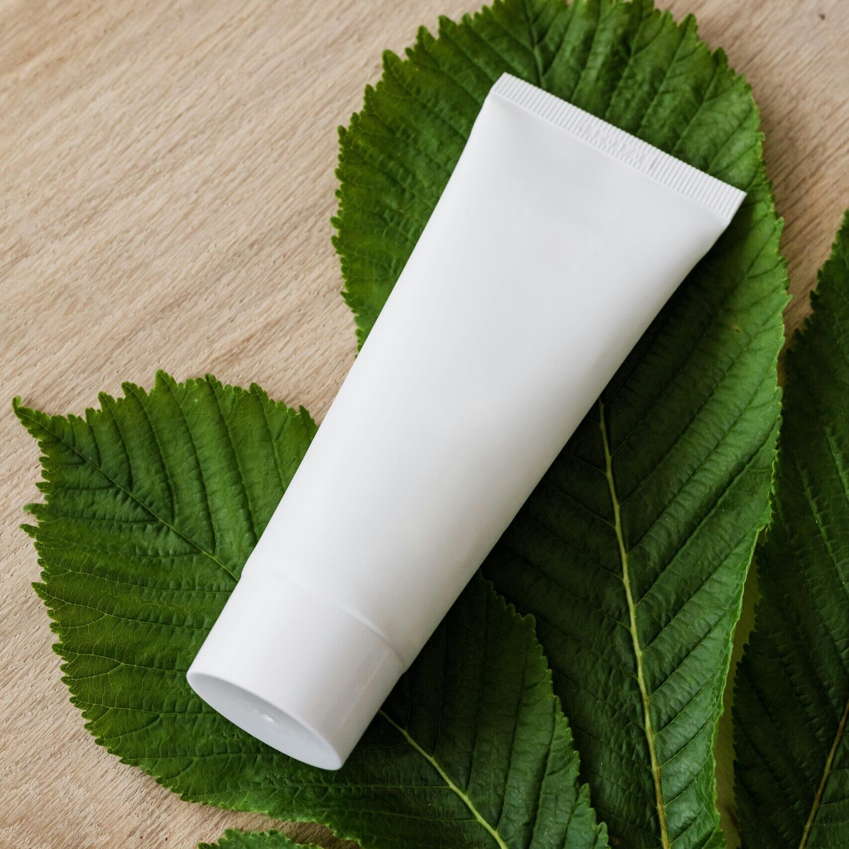 White cosmetic tube on lush green leaves promoting natural skincare.